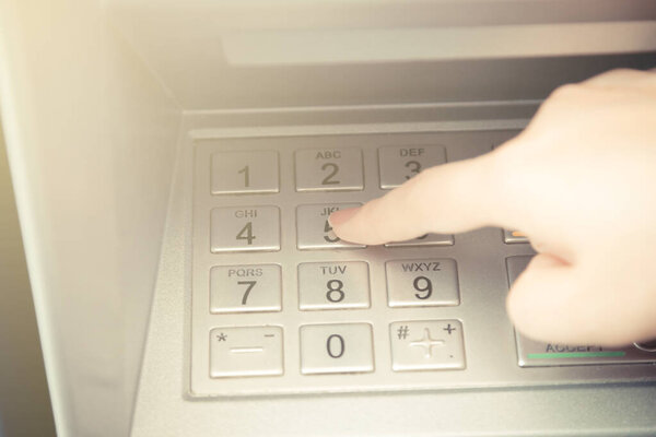 Close up of hand entering pin code at ATM machine to withdraw her money