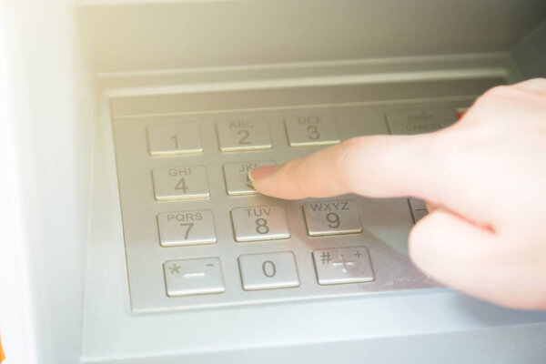 Close up of hand entering pin code at ATM machine to withdraw her money