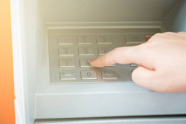 Close up of hand entering pin code at ATM machine to withdraw her money