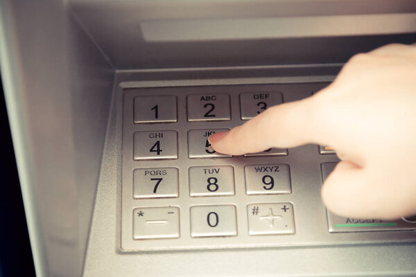 Close up of hand entering pin code at ATM machine to withdraw her money