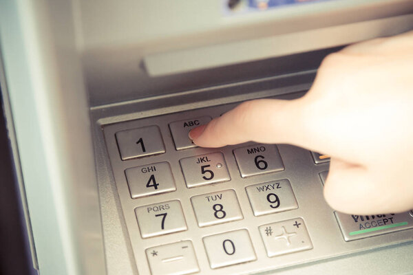 Close up of hand entering pin code at ATM machine to withdraw her money