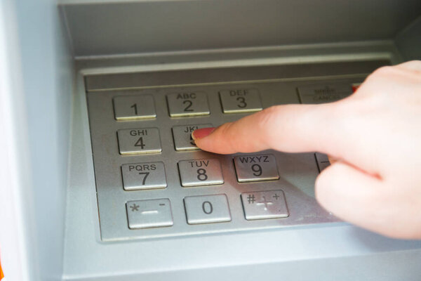 Close up of hand entering pin code at ATM machine to withdraw her money