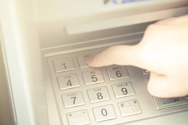 Close up of hand entering pin code at ATM machine to withdraw her money