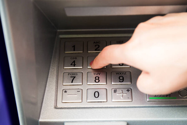 Close up of hand entering pin code at ATM machine to withdraw her money
