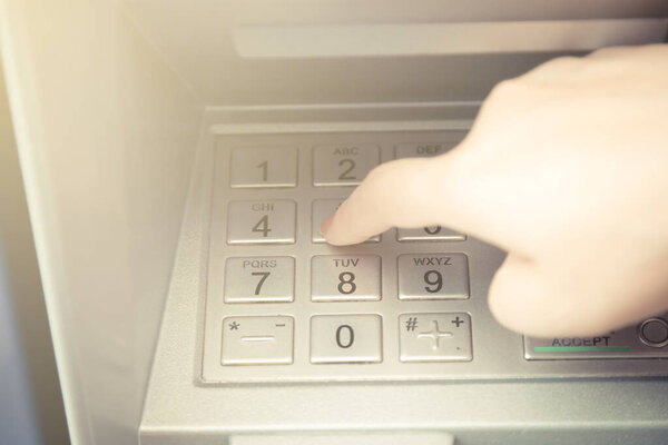 Close up of hand entering pin code at ATM machine to withdraw her money