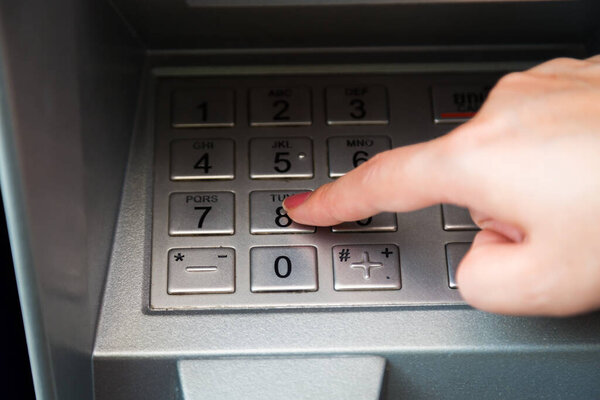 Close up of hand entering pin code at ATM machine to withdraw her money