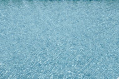 Parıldayan yansımaları ve güneş ışığı altında dalgalanmaları olan canlı mavi su yüzeyi.