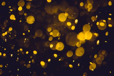 Koyu bir arka planda farklı boyut ve renklerde odanmamış altın bokeh ışıkları.