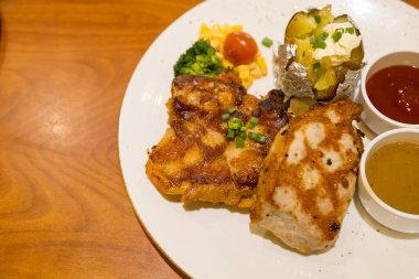 Izgara domuz bifteği, patates püresi ve sebzeyle servis edilir.