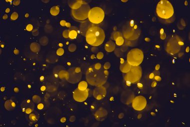 Koyu bir arka planda farklı boyut ve renklerde odanmamış altın bokeh ışıkları.
