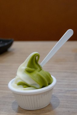 Küçük bir fincan kıvrımlı kibrit ve vanilyalı dondurma, beyaz plastik bir kaşık ve ahşap bir masa..