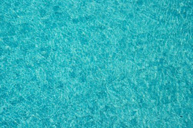 Parıldayan yansımaları ve güneş ışığı altında dalgalanmaları olan canlı mavi su yüzeyi.