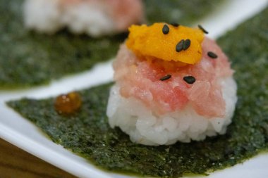 İki tane baharatlı ton balıklı suşi ısırığı, bir parça uni (deniz kestanesi) ve siyah susam tohumları, nori ve beyaz bir tabak..