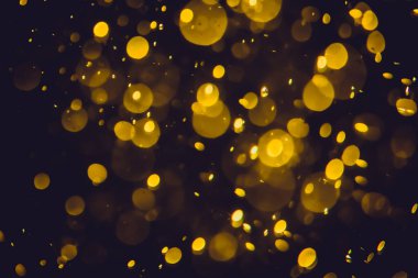 Koyu bir arka planda farklı boyut ve renklerde odanmamış altın bokeh ışıkları.
