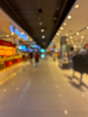 Çağdaş bir alışveriş merkezinde ya da büyük bir perakende mağazasında renkli ışıkları olan geniş, aydınlık bir koridorda yürüyen insanların bulanık görüntüsü.
