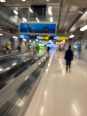 Havaalanı terminali boyunca yürüyen bir yürüyüş yolu ve modern mimari detaylarla yürüyen gezginlerin bulanık görüntüsü.