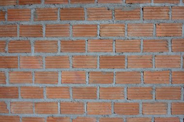 Gri harç ve çelik takviye çubukları (inşaat çubuğu) ile kısmen inşa edilmiş kırmızı tuğla bir duvar, devam eden bir inşaat sürecini işaret ediyor.