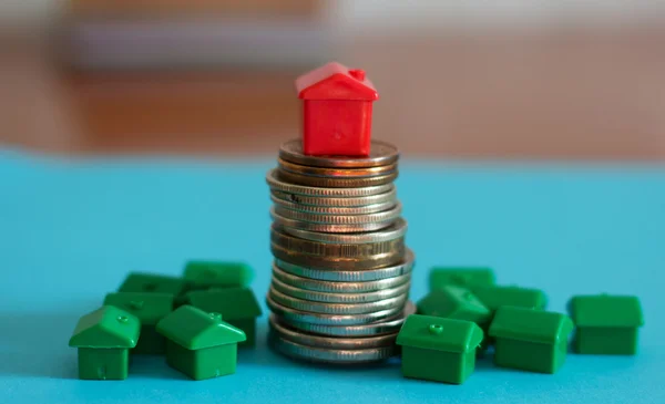 Pequeño modelo de casa de plástico en la parte superior de monedas apiladas . — Foto de Stock