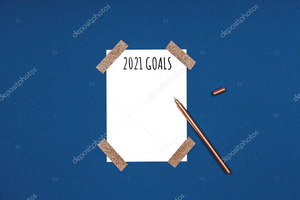 Clean and stylish isolated white card with 2021 goals wording and golden pen. Flat lay background in gold and classic blue colors for any celebration and party occasion