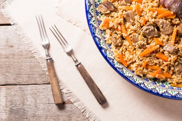 Pilaf in handmade plate on wooden background — Stock Photo, Image