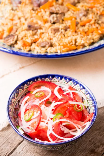 Pilaf and achichuk salad in handmade plate on wooden background — Stock Photo, Image