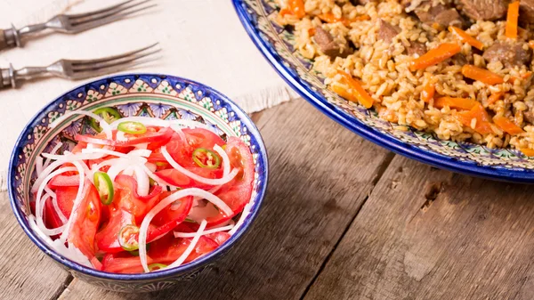 Pilaf and achichuk salad in handmade plate on wooden background — Stock Photo, Image