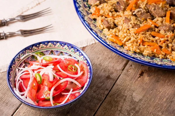 Pilaf and achichuk salad in handmade plate on wooden background — Stock Photo, Image