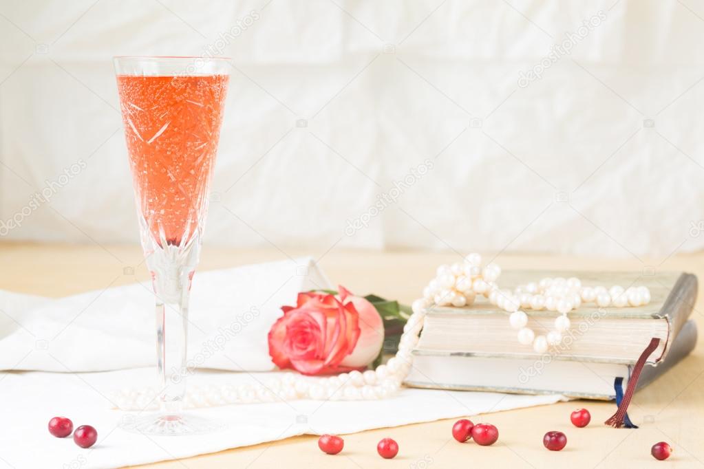 Glass of kir royal cocktail with vintage books and pearls