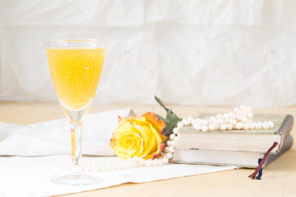 Glass of mimosa cocktail with vintage books and pearls