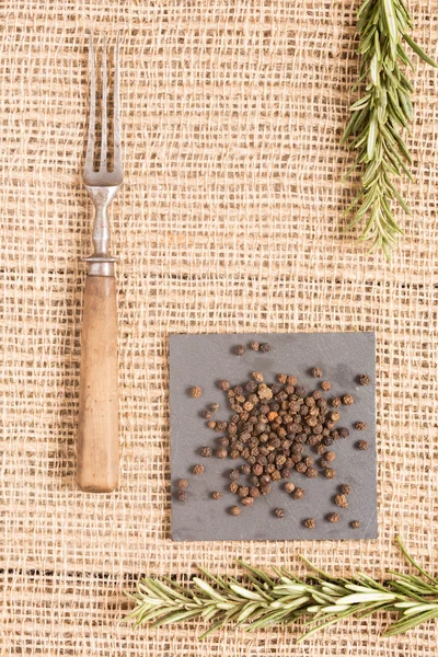 Pimienta negra en platos oscuros con romero y tenedor antiguo — Foto de Stock