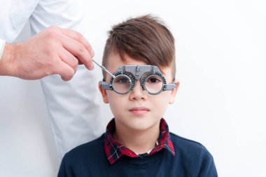 Gözlüklü bir çocuk göz doktoruna bakıyor.