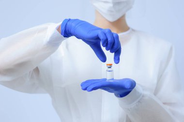 Eldivenli ve maskeli bir doktor elinde aşı tutuyor.