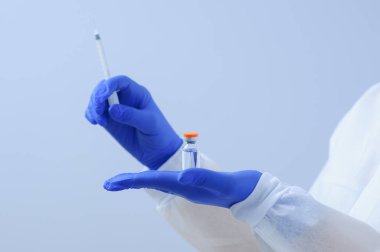 Eldivenli ve maskeli bir doktor elinde aşı tutuyor.