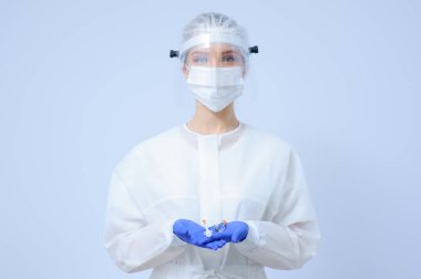 Eldivenli ve maskeli bir doktor elinde aşı tutuyor.
