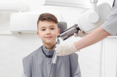 Diş hekimi elleri, diş kliniğindeki küçük çocuk için çene röntgeni görüntüsü oluşturur