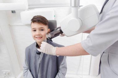 Diş hekimi elleri, diş kliniğindeki küçük çocuk için çene röntgeni görüntüsü oluşturur