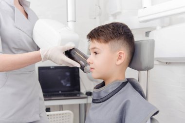 Diş hekimi elleri, diş kliniğindeki küçük çocuk için çene röntgeni görüntüsü oluşturur
