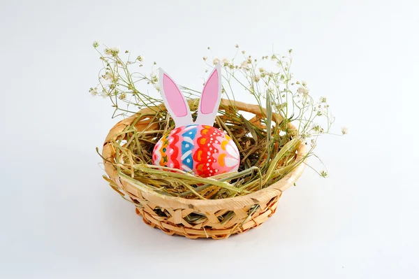 Huevo de Pascua en una canasta con heno sobre fondo blanco — Foto de Stock