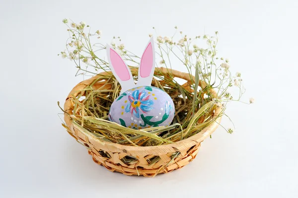 Huevo de Pascua en una canasta con heno sobre fondo blanco — Foto de Stock