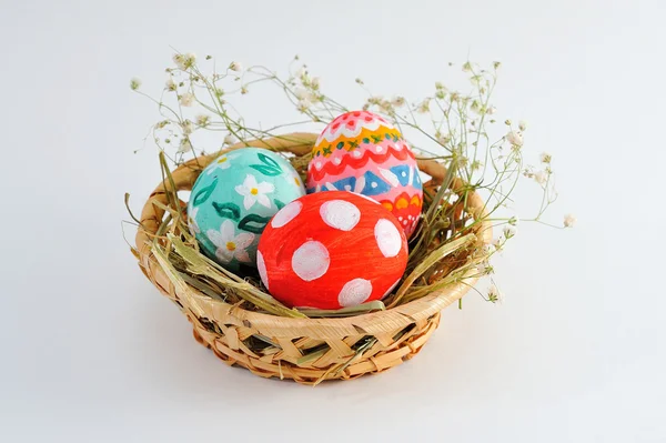 Huevos de Pascua en una canasta con heno sobre fondo blanco — Foto de Stock