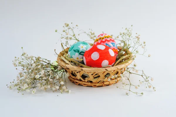 Huevos de Pascua en una canasta con heno sobre fondo blanco — Foto de Stock
