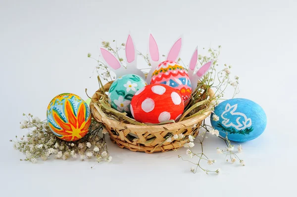 Huevos de Pascua en una canasta con heno sobre fondo blanco — Foto de Stock