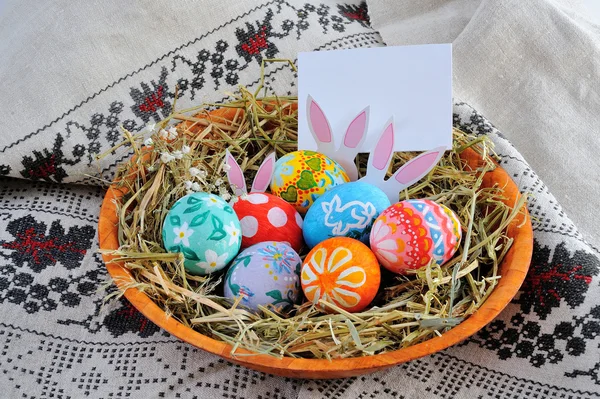 Huevos de Pascua en un plato con heno sobre fondo de lino — Foto de Stock