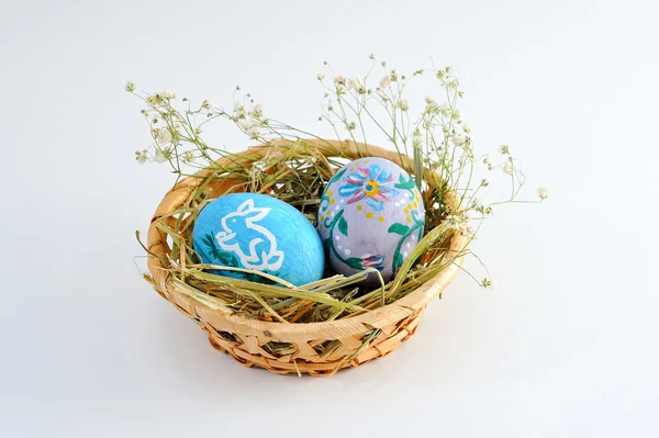 Huevos de Pascua en una canasta con heno sobre fondo blanco — Foto de Stock