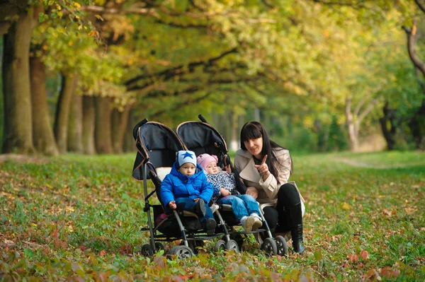 Madre con niños gemelos en un paseo por el parque de otoño — Foto de Stock