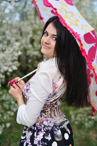Cute dziewczyna dosiada ogród wiosną pod parasolem — Zdjęcie stockowe