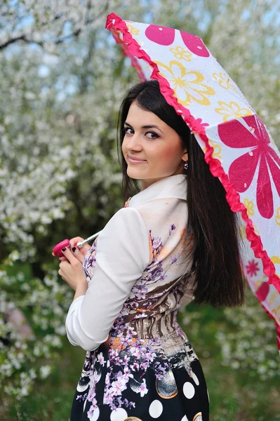 Menina bonito caminha no jardim de primavera sob um guarda-chuva — Fotografia de Stock