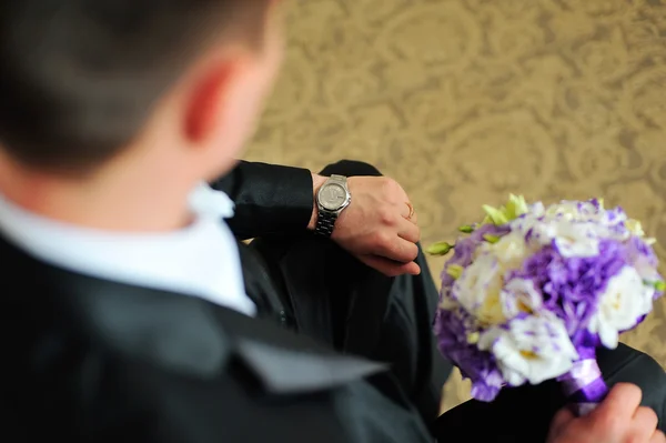 Sposo guardando il suo orologio con un bouquet tra le mani — Foto Stock