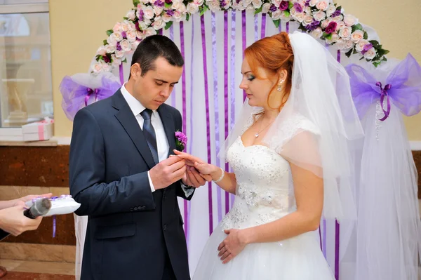 Groom putting ring on bride's finger under the arch — Stock Photo, Image