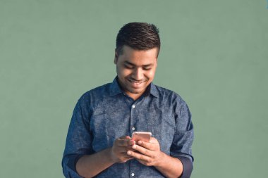 Genç Hintli adam gülümsüyor ve işaret parmağıyla işaret ediyor yarı günlük giysiler içinde açık mavi arka planda yalnız poz veriyor.